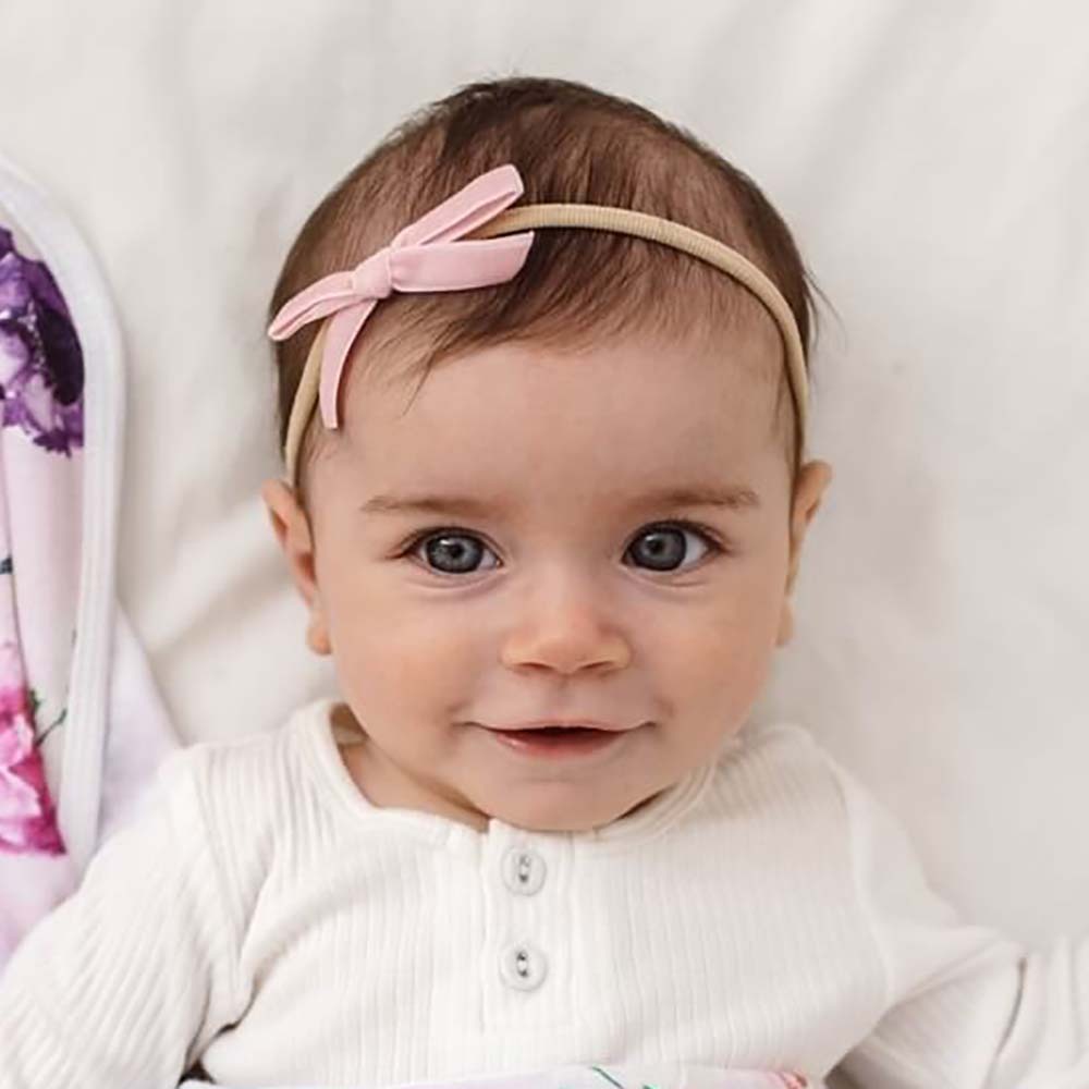 Baby wearing a white outfit with a pink headband on a light background