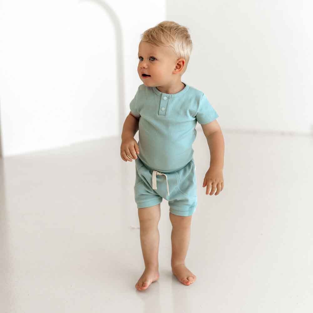 Child wearing a light green outfit standing on a white surface