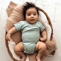Baby in a light blue onesie lying on a woven basket with a pink blanket