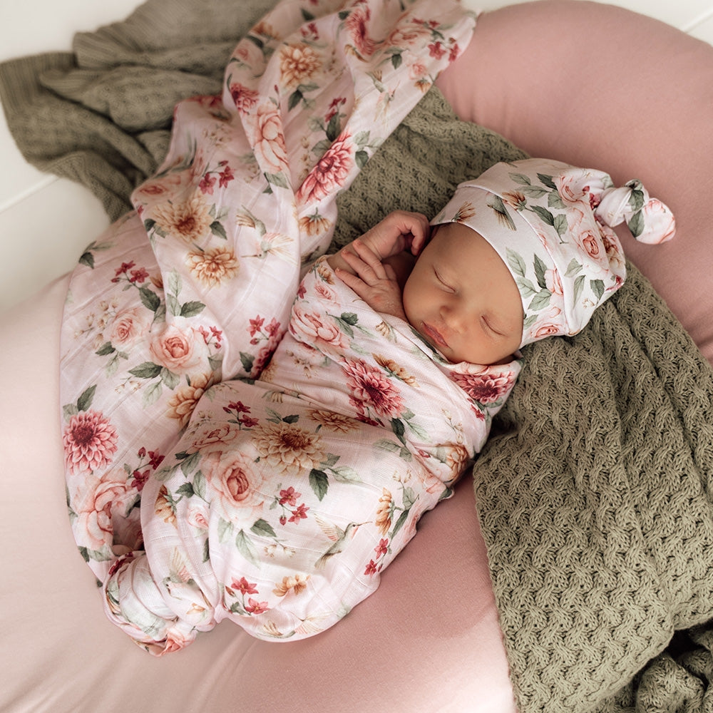 Newborn baby wrapped in a floral blanket with a matching headband, lying on a green textured blanket.