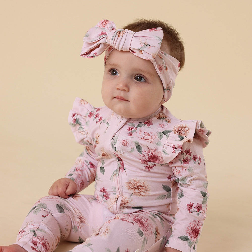Baby in floral outfit with matching headband on a beige background