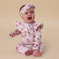 Baby wearing a floral outfit and headband on a beige background