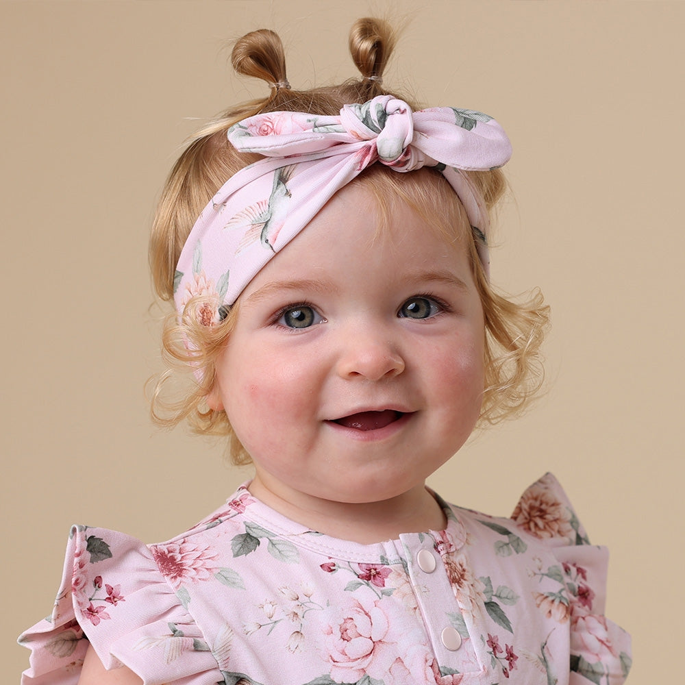 Baby wearing a floral headband and outfit against a beige background