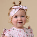 Baby wearing a floral headband and outfit against a beige background