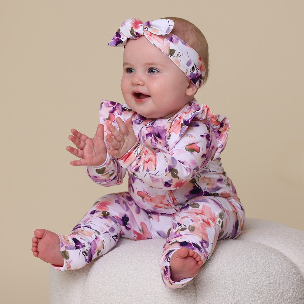 Baby in a floral outfit with a matching headband on a beige background