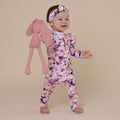 Baby in a floral onesie holding a pink bunny toy on a beige background