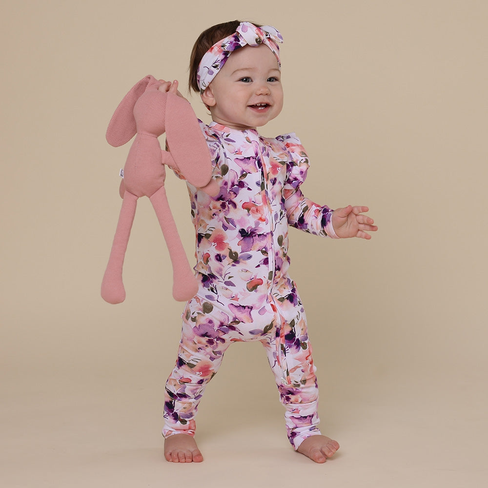 Baby in a floral onesie holding a pink bunny toy on a beige background
