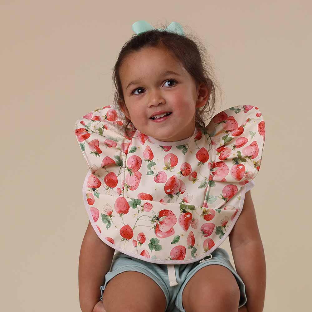 Young girl wearing Snuggle Hunny strawberry patterned feeding bib from Meridian Baby