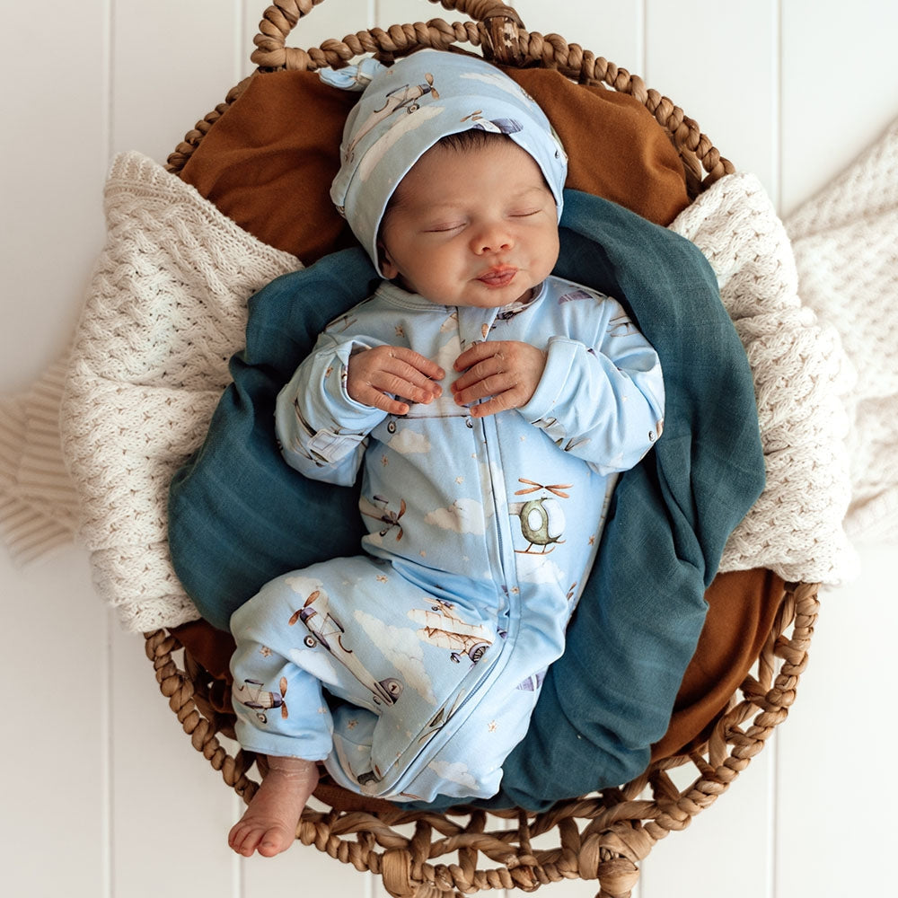 Newborn baby in a blue outfit with airplane patterns, sleeping in a woven basket.