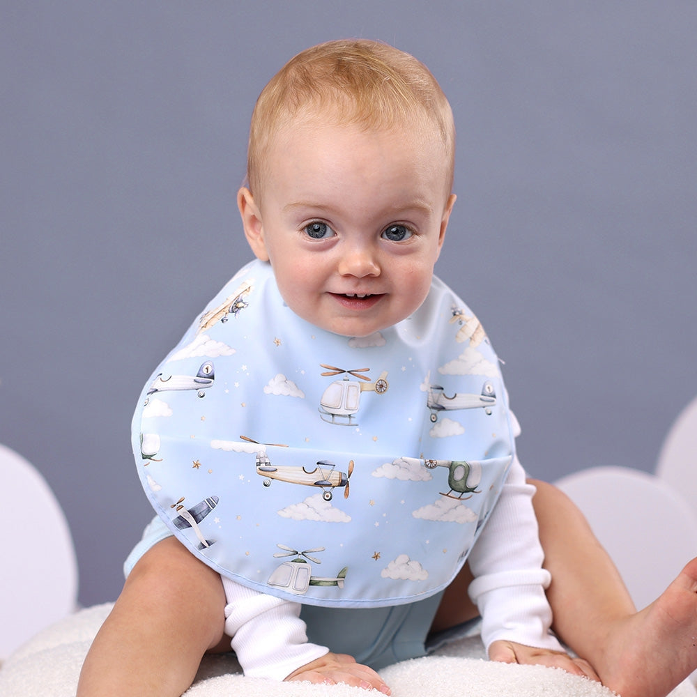 Baby boy wearing blue Snuggle Hunny feeding bib with airplane designs from Meridian Baby.