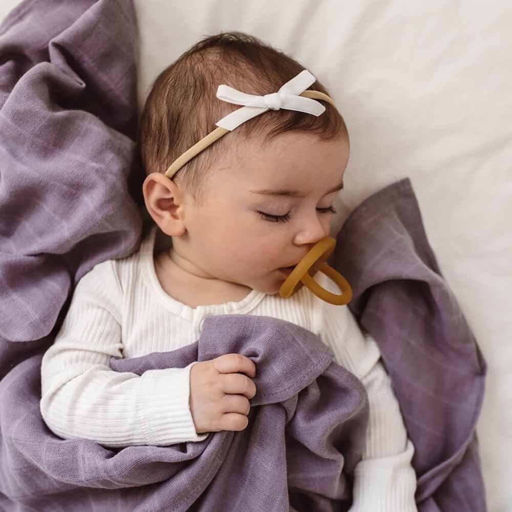Baby with a pacifier lying on a purple blanket