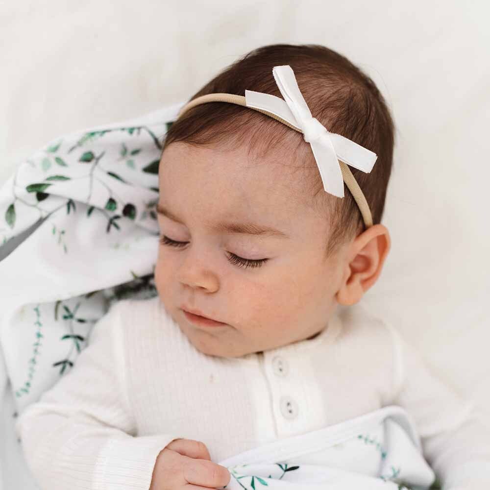 Baby wearing a white headband with a bow, surrounded by green and white fabric